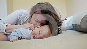 Beautiful curly woman kisses and hugs a one-year-old child. Mother and child tickles and laughs