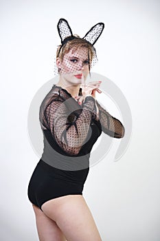 Beautiful curvaceous girl in a transparent elegant mask of a hare with ears and in a black body with lace on a white background in