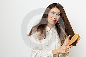 beautiful, cute, attractive middle-aged brunette combing her long hair with a wooden comb while standing in a white