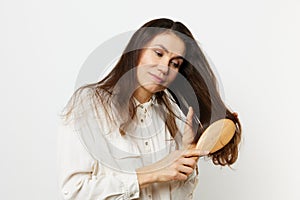 beautiful, cute, attractive middle-aged brunette combing her long hair with a wooden comb while standing in a white