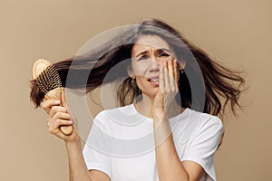 beautiful, cute, attractive middle-aged brunette combs her long hair with a wooden comb while standing in a white poppy