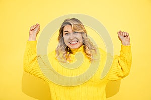 Beautiful cute blond hair young blonde woman wearing yellow sweater over isolated yellow wall background excited, success, arms