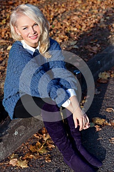 Beautiful cute blonde girl in a blue jacket sitting on the road in the autumn Park
