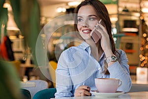 Beautiful cute caucasian young woman in the cafe, using mobile phone and drinking coffee smiling
