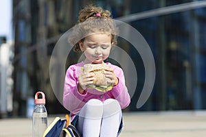 Beautiful cute child with appetite eating fast food, portrait. happy girl biting homemade sandwich.