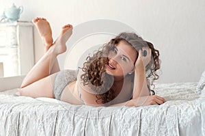 beautiful cute curly smiling female lying on the bed legs crossed