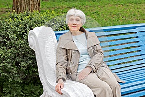 Beautiful cute elderly woman sitting on park bench blue