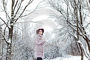 Beautiful cute elegant girl in a fur coat and hat walking in the winter forest bright frosty morning