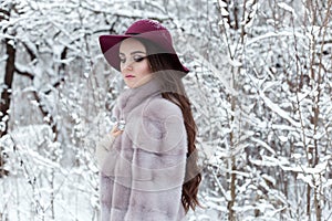 Beautiful cute elegant girl in a fur coat and hat walking in the winter forest bright frosty morning