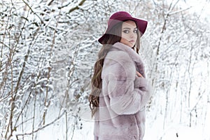 Beautiful cute elegant girl in a fur coat and hat walking in the winter forest bright frosty morning