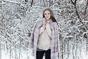 Beautiful cute elegant girl in a fur coat walks in the winter forest bright frosty morning