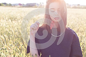 Beautiful cute girl with big lips and red lipstick in a black jacket with a flower poppy standing in a poppy field at sunset