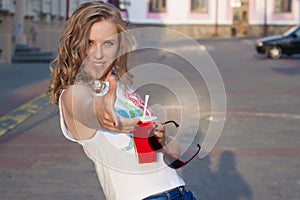 Beautiful cute girl with curly hair in sunglasses with a paper glass and a straw drinking a drink in the city on a sunny summer ev