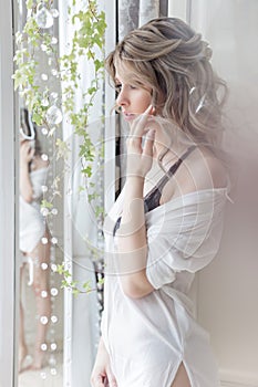 Beautiful cute girl near the window in the morning in a white shirt with a cup of coffee