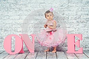 Beautiful and cute girl in a pink dress with the letters one on her first birthday. Emotional girl.