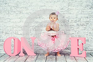 Beautiful and cute girl in a pink dress with the letters one on her first birthday. Emotional girl.
