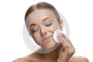 Beautiful cute girl touch her clean face with cotton pad. Young woman with closed eyes.