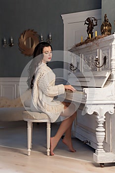 Beautiful cute girl in white warm jacket at home playing on old piano