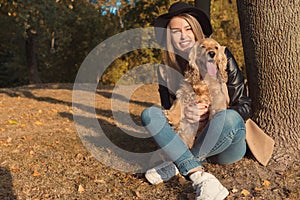 Beautiful cute happy girl in a black hat playing with her dog in a park in autumn another sunny day