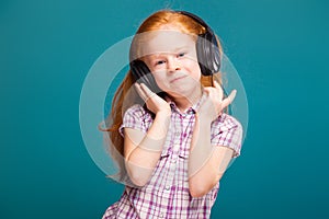 Beautiful, cute little girl in checkered shirt and earphones with long red hair listen to musik