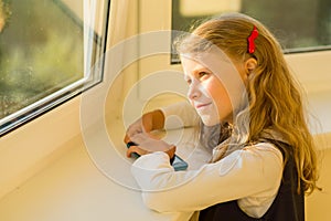 Beautiful cute little girl dressed in school uniform looking out the window