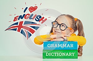 Beautiful cute little girl leaning on thick books,  happily looking at i love English text and UK flag above her head