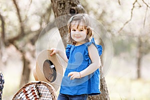 A beautiful cute little girl smiles and has fun in a blue blouse with moms hat in a spring garden