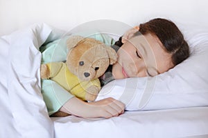 Beautiful cute little girl with a toy teddy bear sleeps in her bed, smiling sweetly