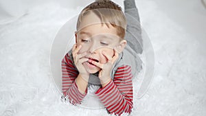 Beautiful cute preschool child plays lying on his stomach and waving his legs. The boy is smiling at the camera close-up