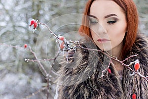Beautiful cute young girl with red hair walking in a snowy forest among the trees missed first trimester bushes with red yago
