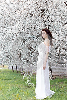 Beautiful cute sweet girl bride with gentle eye make-up full lips in white light dress walks in the lush garden on warm s