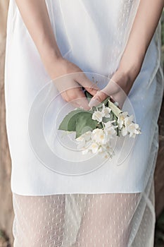 Beautiful cute tender girl with dark hair in a white summer dress with a jasmine flower in hands