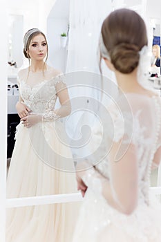 Beautiful cute tender young girl bride in wedding dress in mirrors with evening hair and gentle light make-up