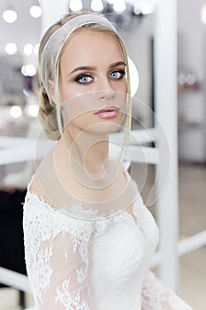 Beautiful cute tender young girl bride in wedding dress in mirrors with evening hair and gentle light make-up