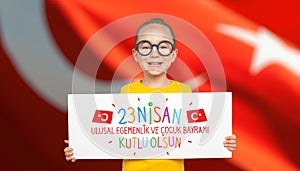 Beautiful cute Turkish girl holding a white paper with national holiday celebration message in front of turkey flag. 23 Nisan Kutl