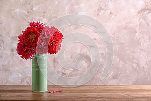 Beautiful dahlia flowers in vase on table against color background.