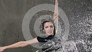 Beautiful dancer girl is performs a jump on the scene under the water rain with splashes of water on her. Modern dance