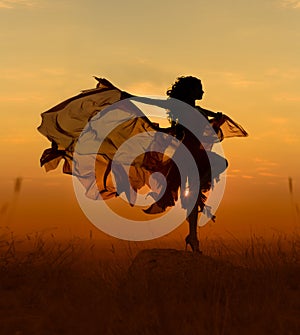 Beautiful dancer woman with flying dress and veil at sunst, orange background.