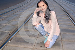 Beautiful dark-haired girl in a blouse and jeans posing on the tram tracks