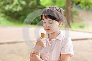 Beautiful dark-haired girl in a dress eats an ice cream cone outdoors