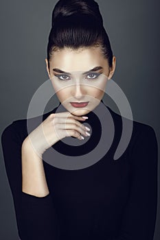 Beautiful dark haired model with perfect make up and her hair scraped back into a high bun leaning her chin on the hand