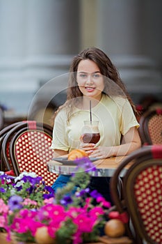 Beautiful dark-haired young curly woman sits in summer cafe and drinks coffee cocktail. Warm. Rest