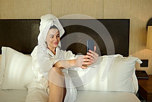 Beautiful dark-haired young woman in white bathrobe and her head wrapped in a towel, relaxing after bathing, lying on a bed in