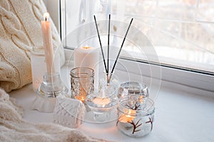 Beautiful decor of white lighted candles in glass candlesticks stand on windowsill, relax place in house, concept of winter cozy