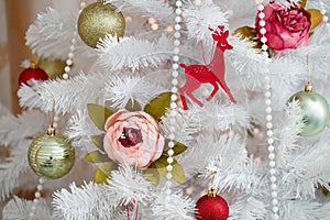 Beautiful decorations are hanging on a white artificial Christmas tree. Green balls, flowers, beads, wooden deer