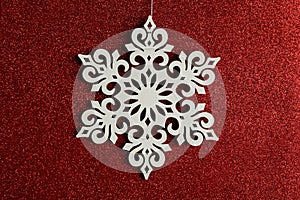 Beautiful decorative snowflake hanging on sparkling red glitter background, closeup