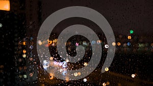 Beautiful defocused bright lights of a big city behind the window with drops of water. Concept. Rain drops on the glass