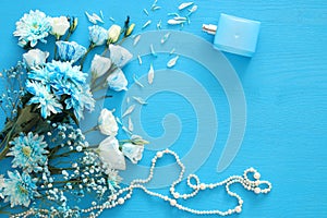 beautiful and delicate blue flowers arrangement next to pearls necklace and fresh perfume