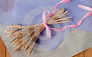 Beautiful delicate bouquet with pink ribbon of dried  wheat ears on the table with a purple sheet of paper and a linen napkin