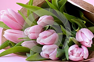 Beautiful delicate bouquet of tulip flowers in craft wrapping paper on pink background